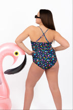 Back view of girl wearing the Coastal Bloom floral one-piece swimsuit with adjustable cross-back straps and full coverage fit while leaning on a pink flamingo inflatable.
