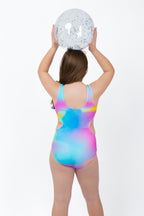 Back view of girl wearing the Cotton Candy Cut-Out rainbow tie-dye one-piece swimsuit with full coverage fit while holding two beach balls.