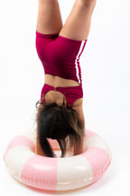 Back view of girl doing a handstand while wearing The OG boy leg one-piece swimsuit in cherry maroon with pink side stripe detail, gold clasp back closure, and full coverage fit.