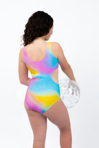 Back view of girl wearing the Cotton Candy Cut-Out rainbow one-piece swimsuit with full coverage fit while holding a beach ball.