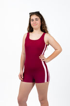 Front view of girl wearing The OG boy leg one-piece swimsuit in cherry maroon with pink side stripe detail and round scoop neckline.