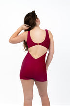 Back view of girl wearing The OG boy leg one-piece swimsuit in cherry maroon with pink side stripe detail, full coverage fit, gold clasp back closure, and open scoop back design.