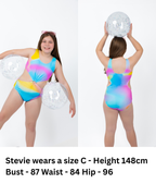 Front and back view of girl wearing the Cotton Candy Cut-Out rainbow one-piece swimsuit with centre ring detail, side cut-outs, and full coverage fit while holding a beach ball.
